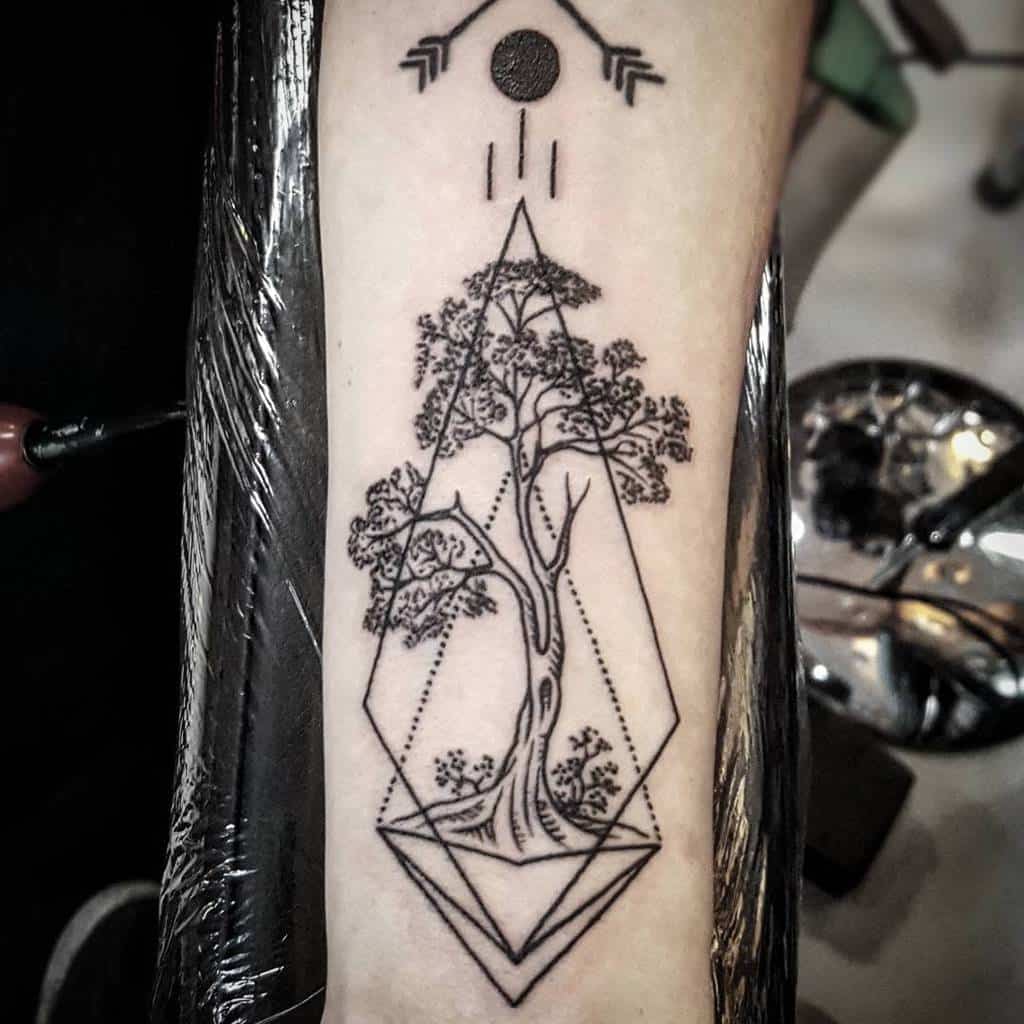 A minimalistic forearm tattoo featuring a tree inside a geometric diamond shape, with arrows and a circle above it