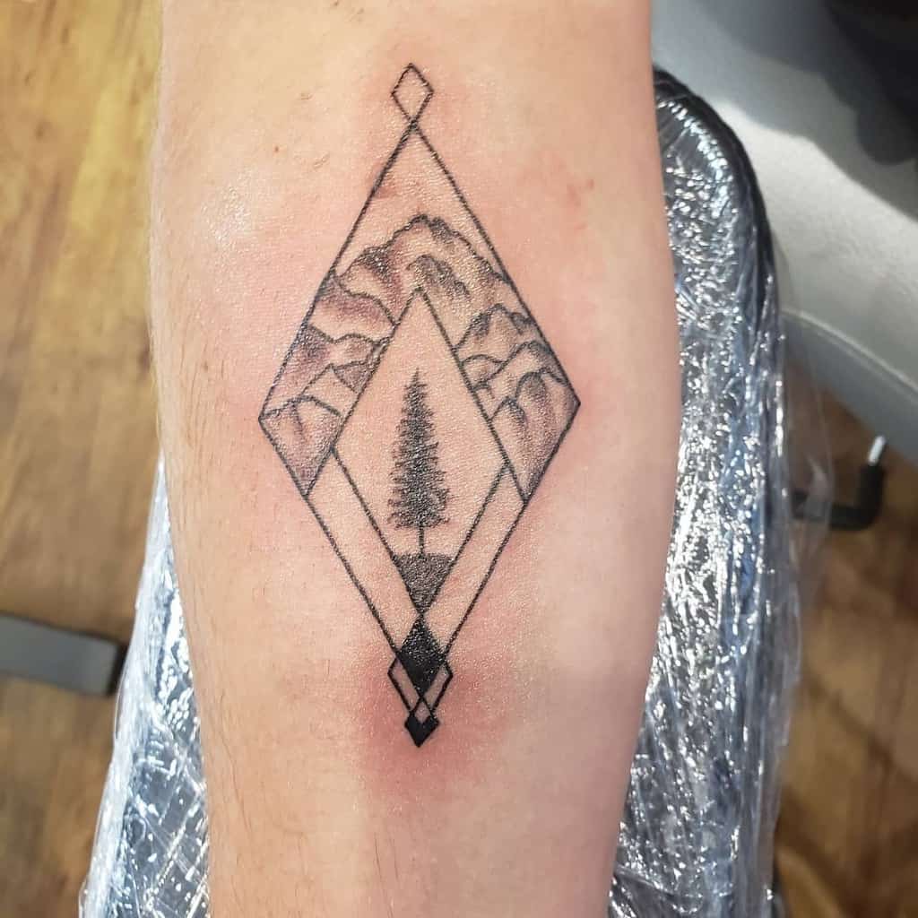 Geometric tattoo with a mountains and tree silhouette inside a diamond shape on an arm