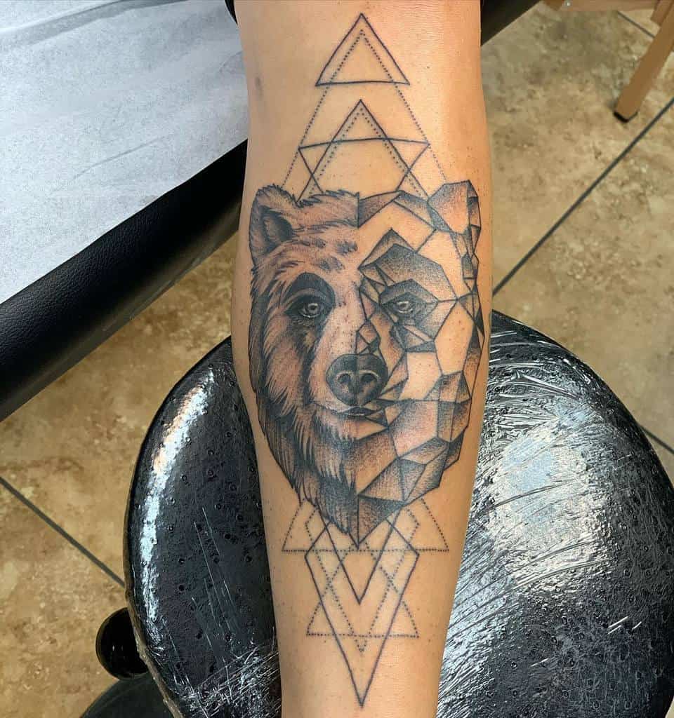A striking bear tattoo graces the leg, masterfully blending realistic and geometric styles, encircled by intricate geometric triangles