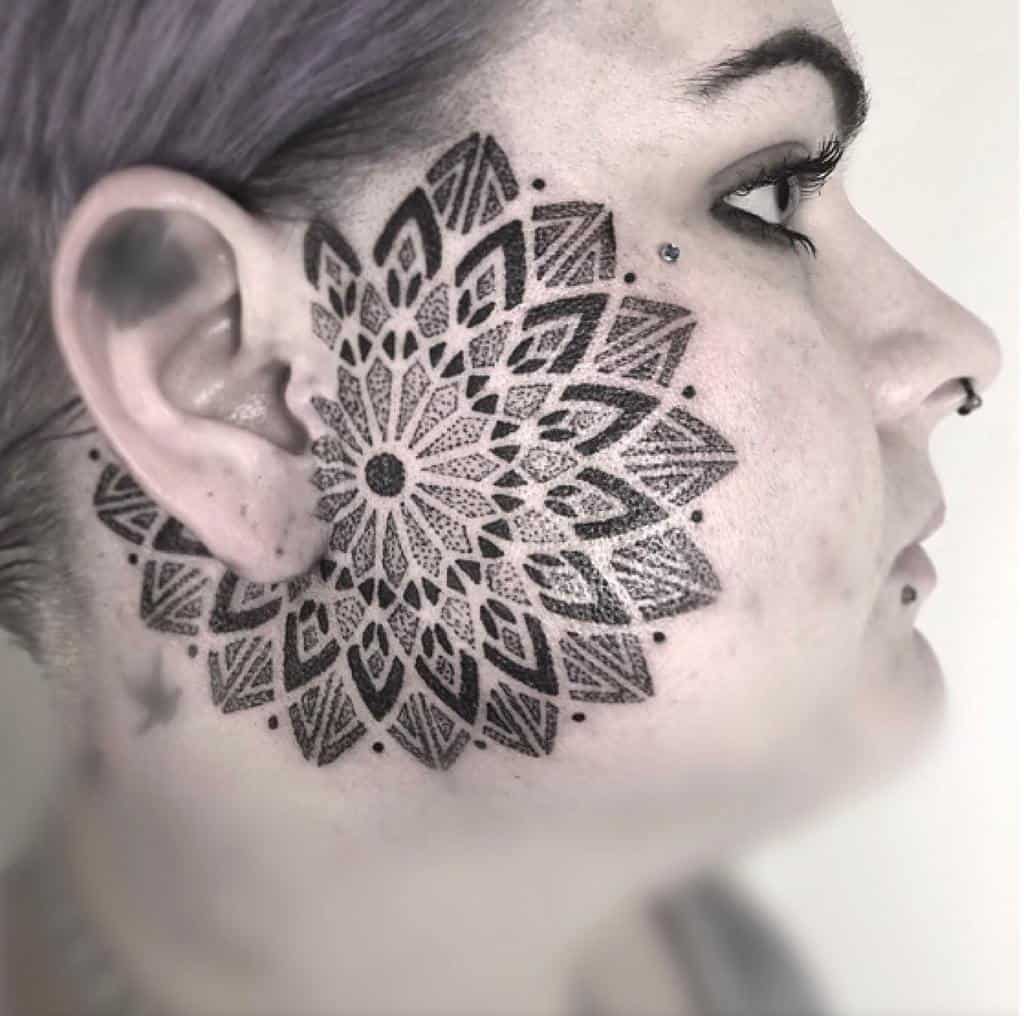 Large, intricate mandala-style tribal tattoo on the cheek, extending from the ear towards the face, featuring detailed geometric patterns and dot work