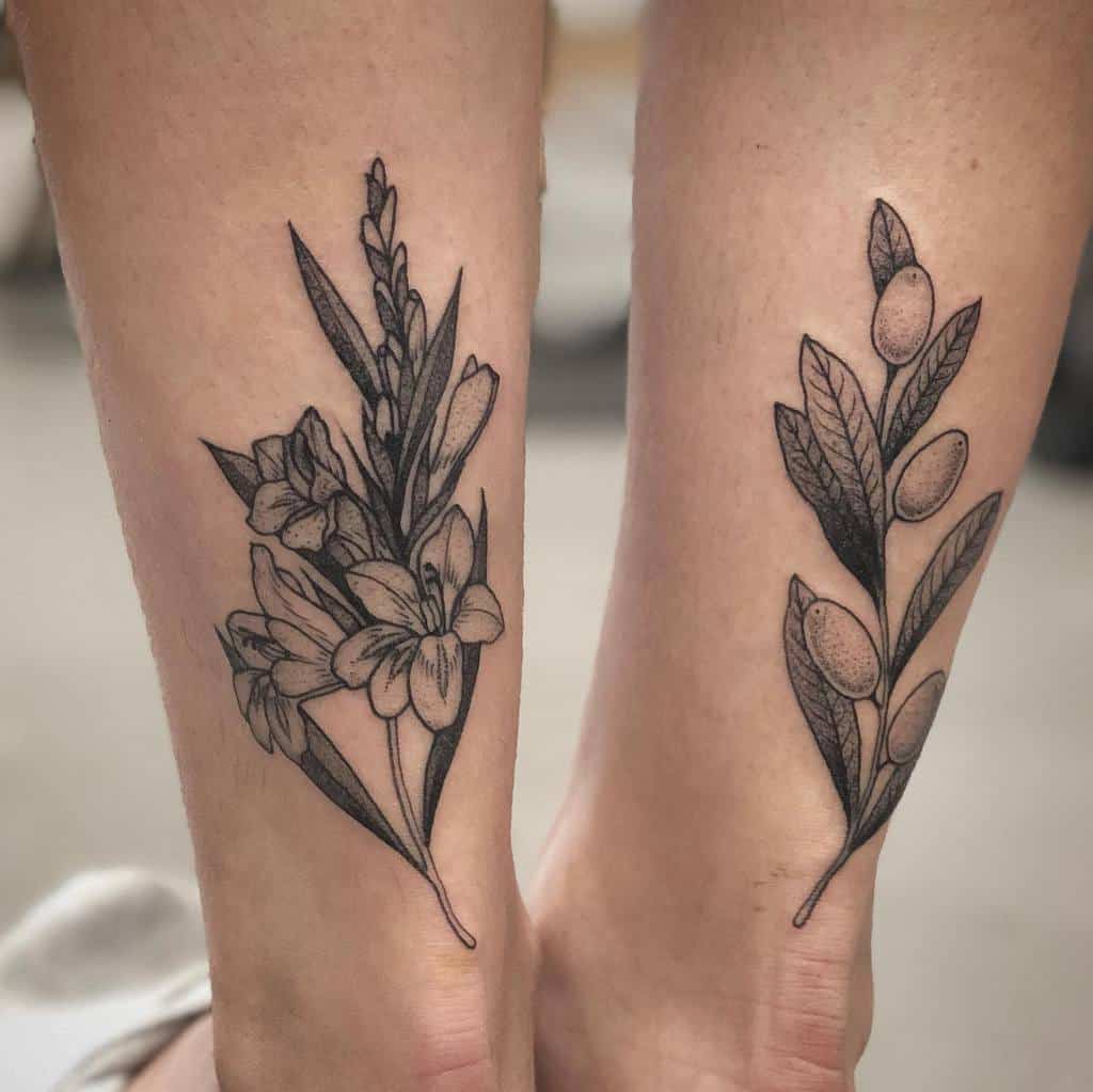 Two legs adorned with detailed floral tattoos; one leg blossoming with gladiolus and flowers, the other flourishing with leaves and berries