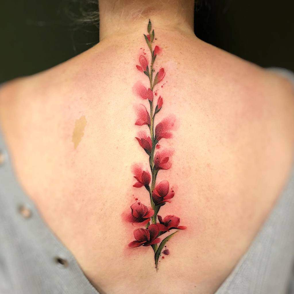 A vibrant vertical gladiolus tattoo, showcasing its stunning pink blooms, adorns a person's back