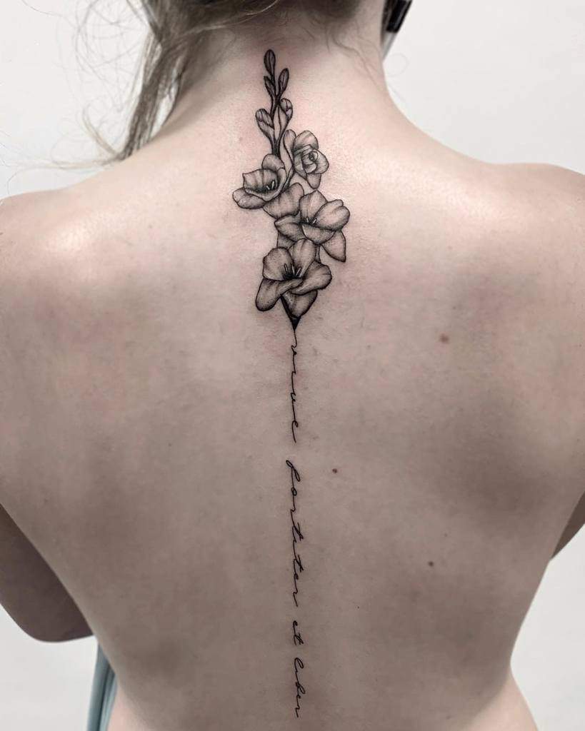 Tattoo of flowers, including a striking gladiolus, with text running down the spine of a person's back