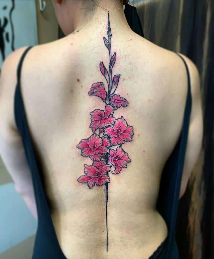 A person with a large tattoo of pink gladiolus flowers along their spine, wearing a black top