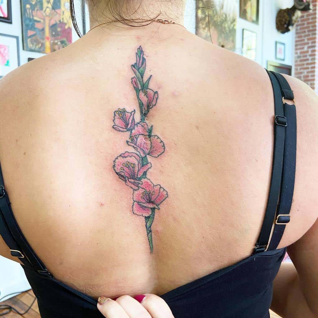 A woman with a pink gladiolus tattoo along her spine