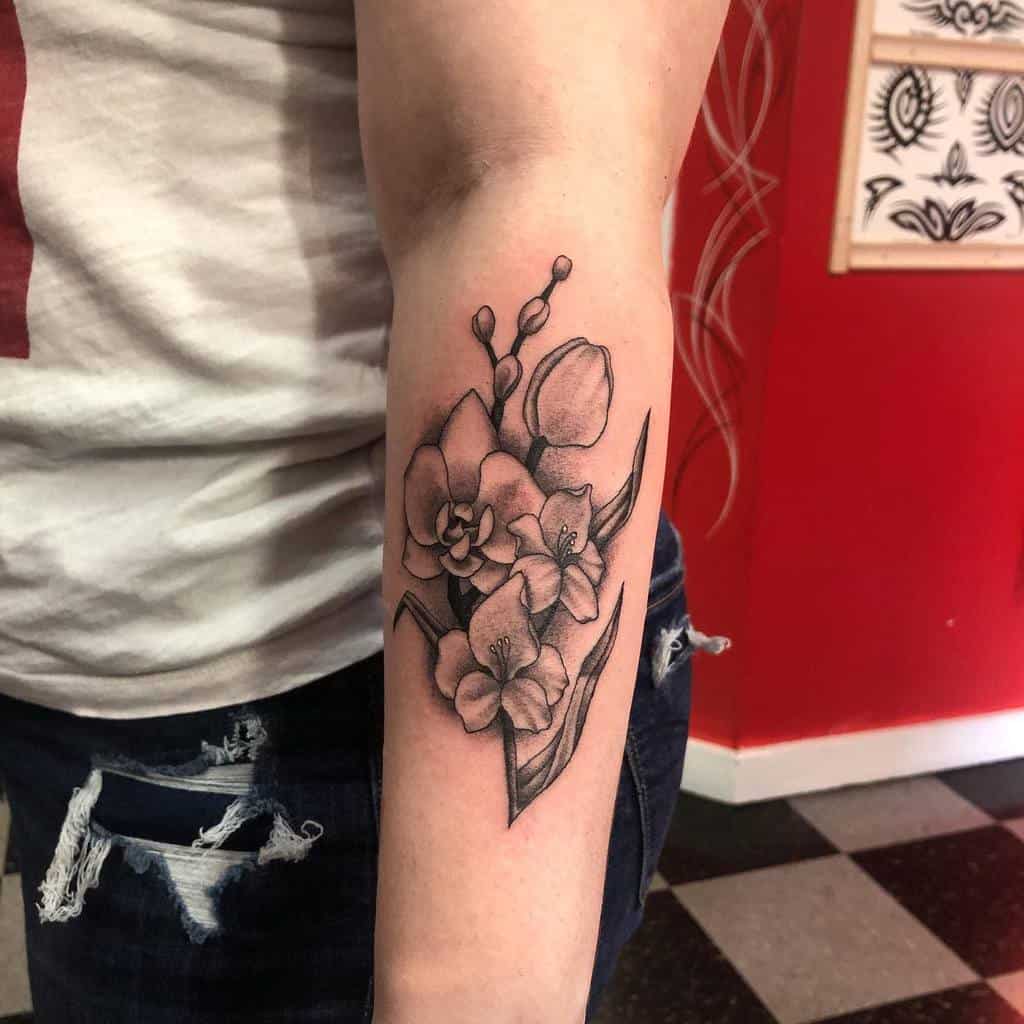 Tattoo of flowers, leaves, and a graceful gladiolus on a person's forearm, with a red wall and art in the background