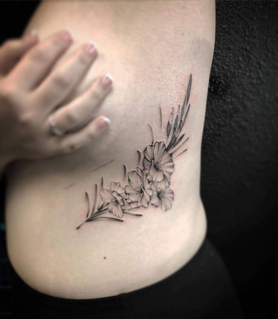 A person with a floral tattoo on their side, showcasing detailed gladiolus flowers and leaves