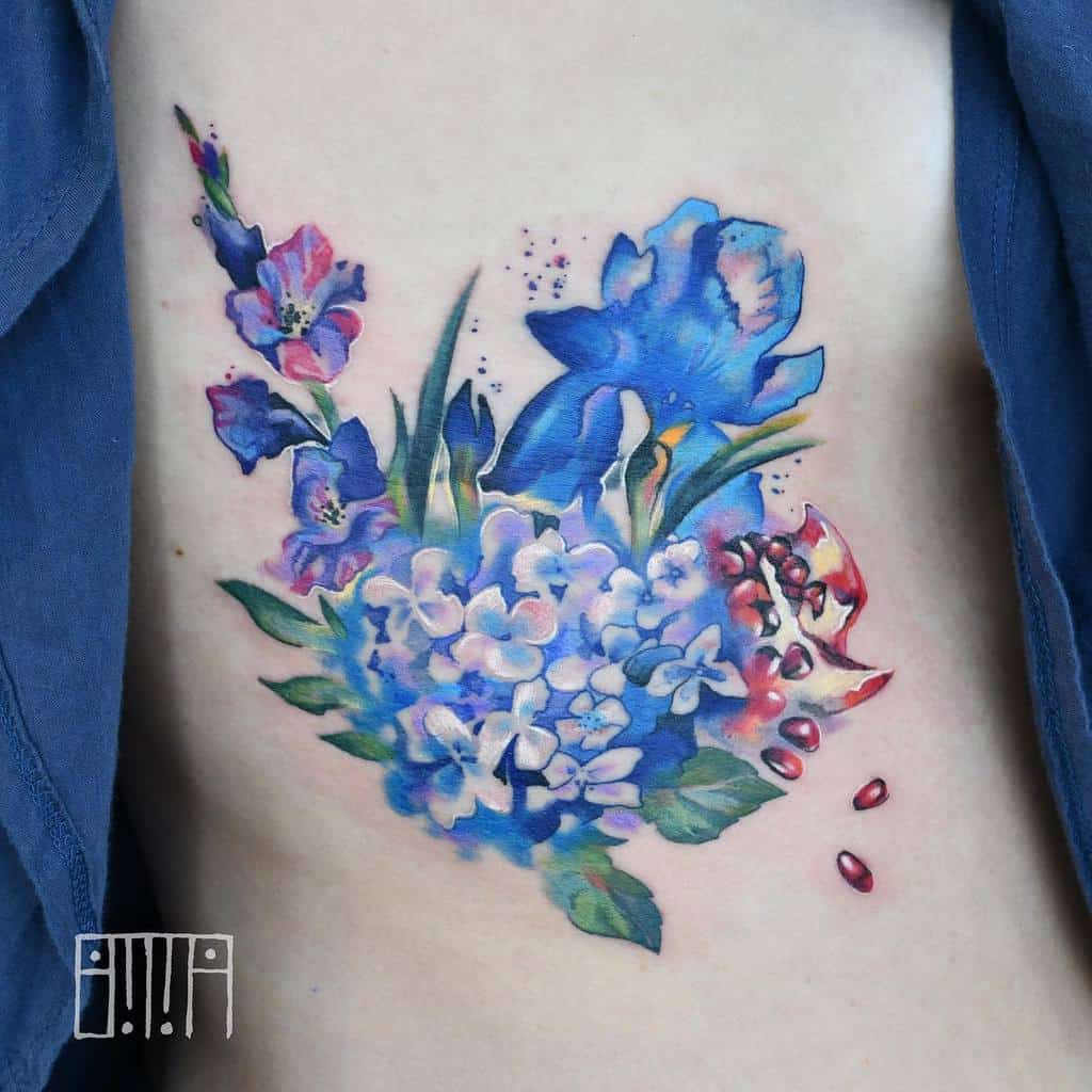 Tattoo of vibrant blue flowers intertwined with pink flowers and a striking gladiolus beside a pomegranate on exposed skin