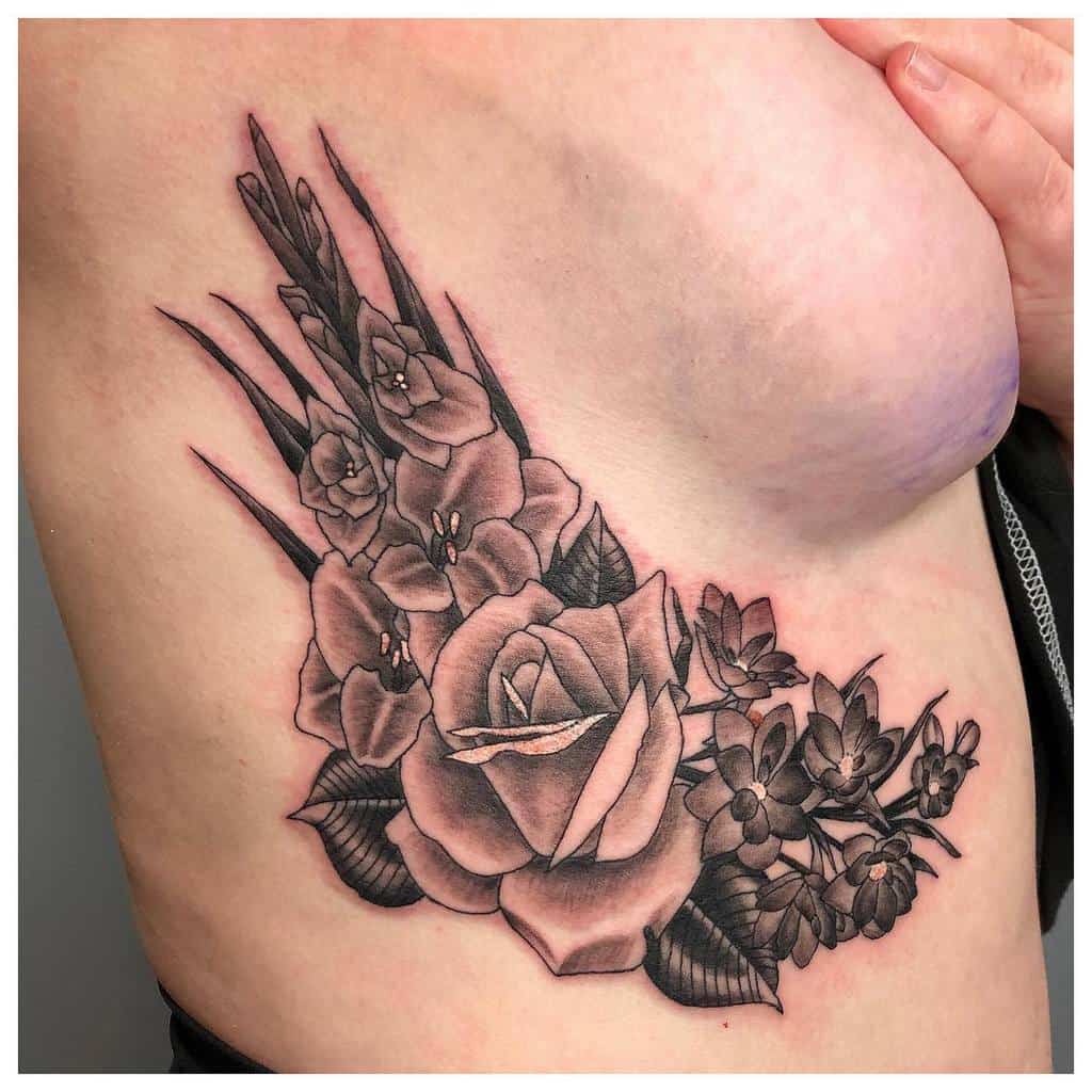 Tattoo of roses, gladiolus, and other flowers on the side of a person's torso, shaded in black and gray