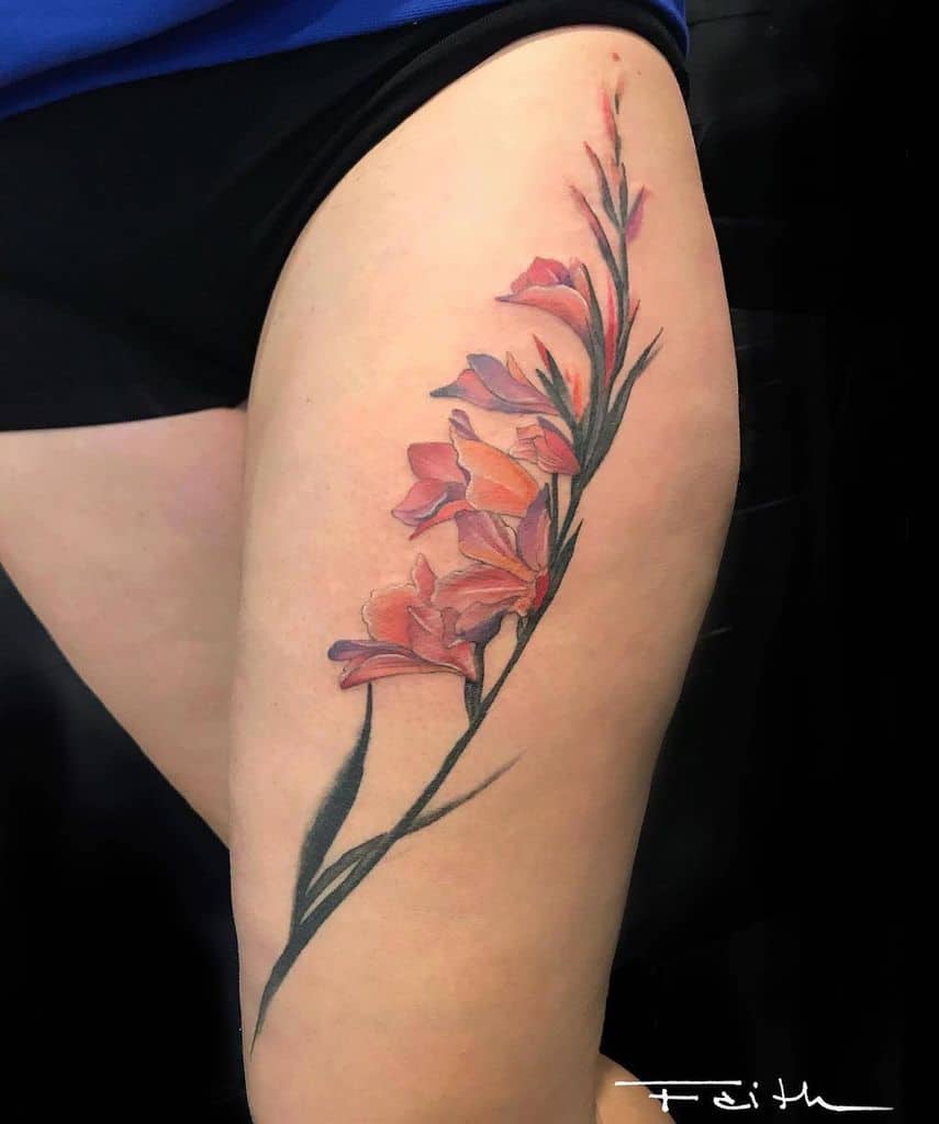 A beautiful tattoo of pink gladiolus flowers runs vertically along the length of a person's thigh