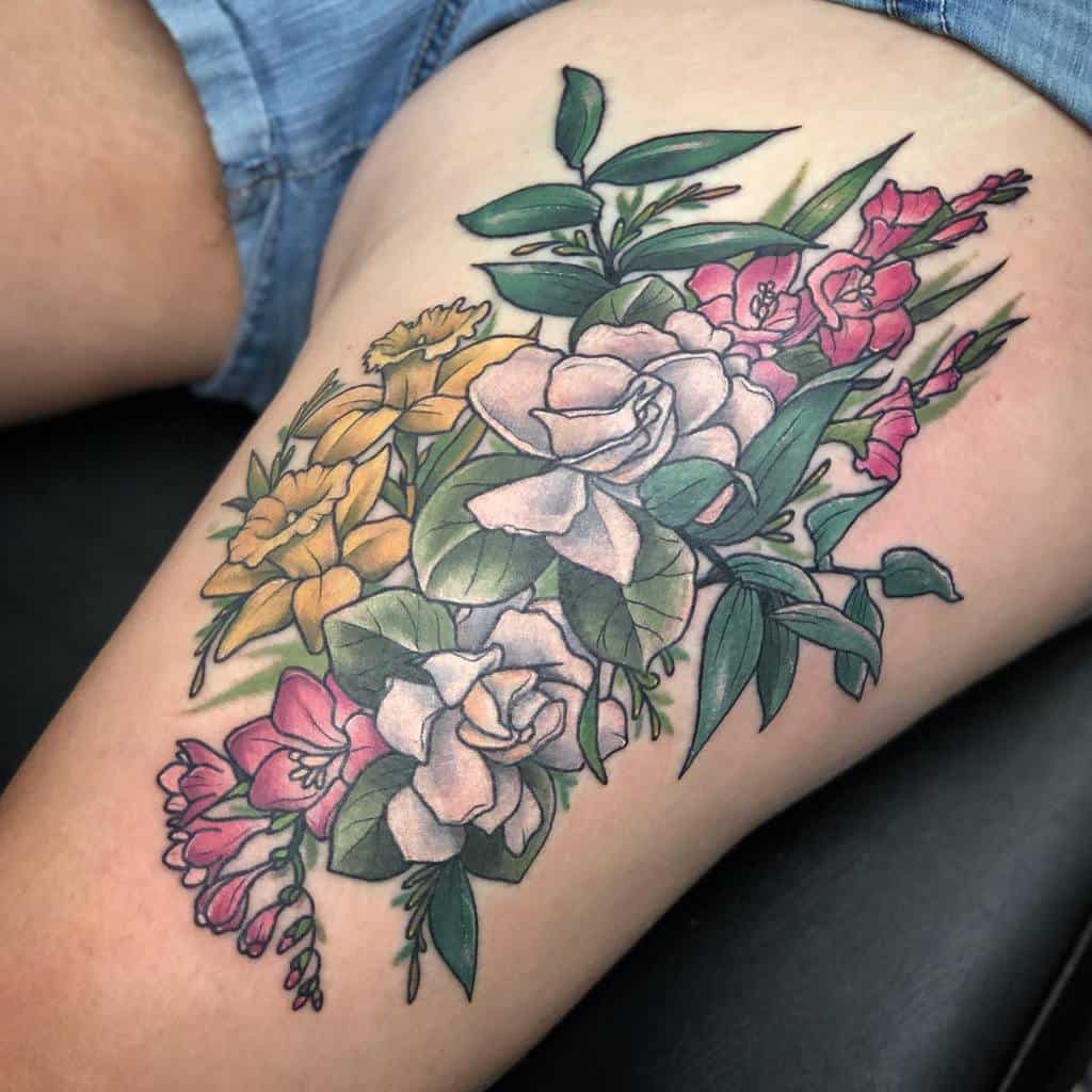 Thigh tattoo of various colorful flowers, including roses, gladiolus, and leaves, on a person wearing shorts