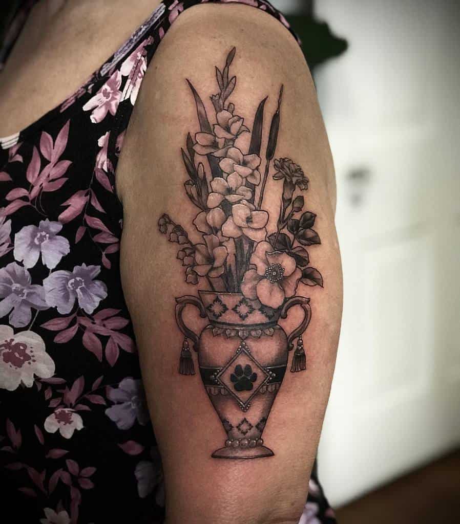 Tattoo of a flower bouquet, including a vibrant gladiolus, in a decorative vase on person's upper arm, wearing floral clothing