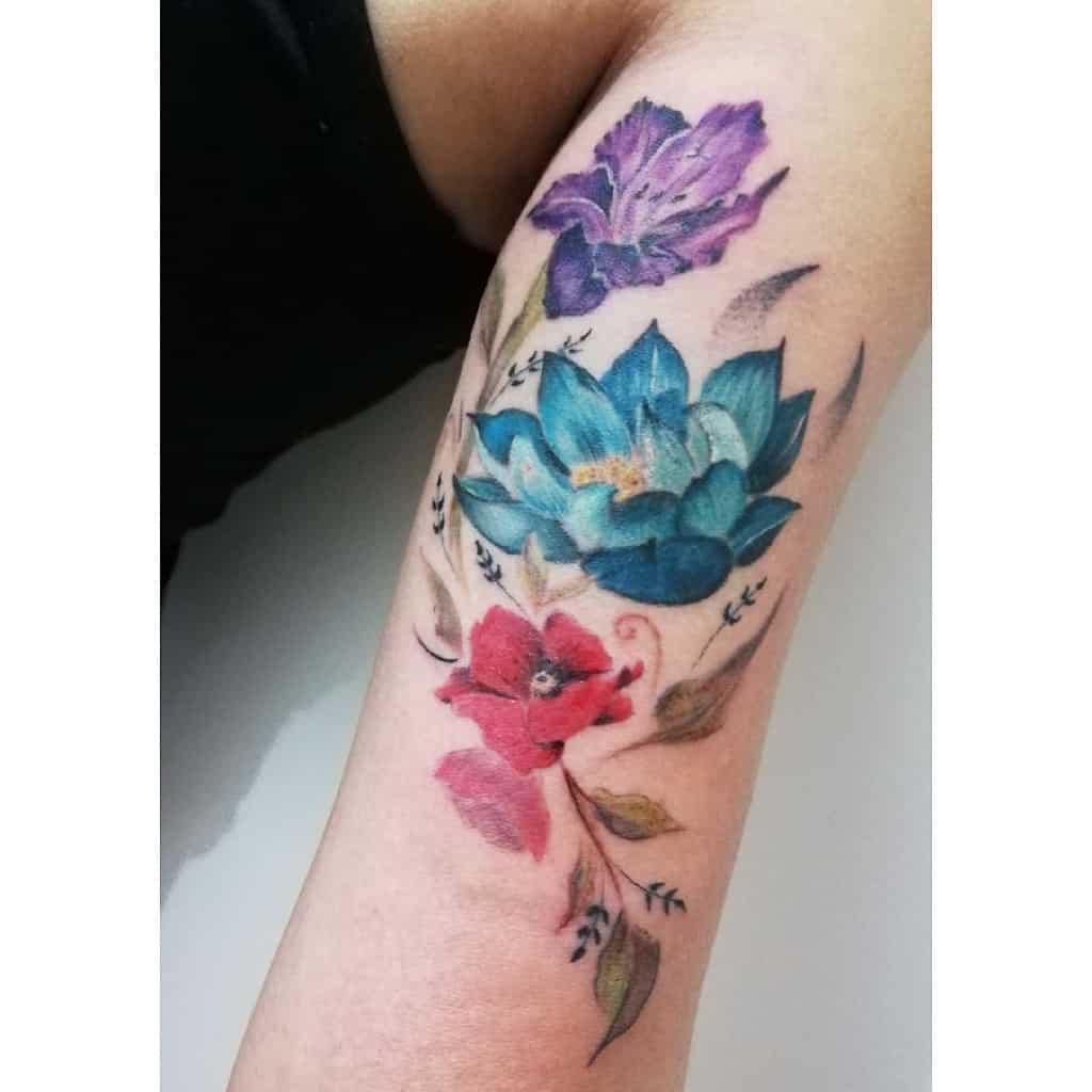 A stunning tattoo of vibrant gladiolus flowers adorns a person's forearm, featuring purple, blue, and red blossoms