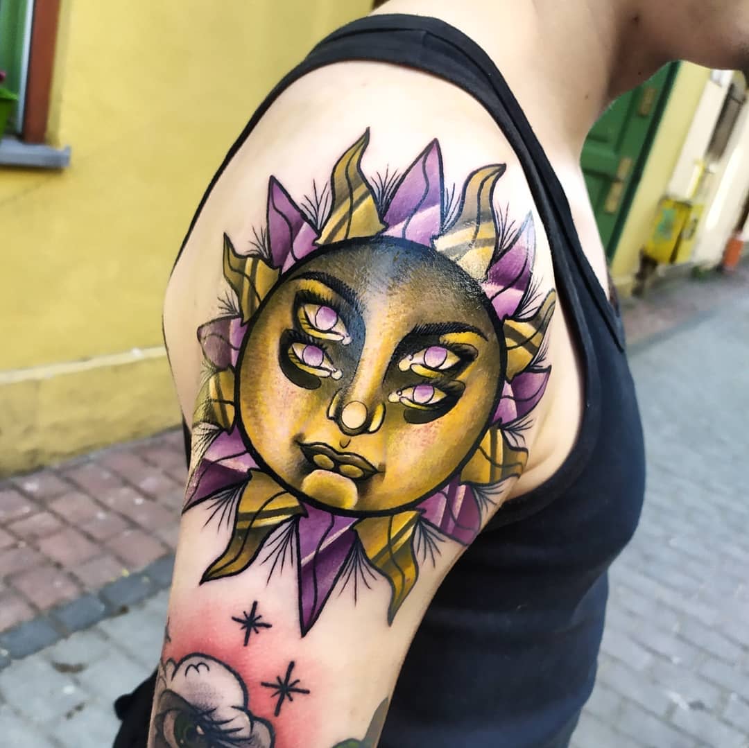 A vibrant sun tattoo with three eyes on an upper arm