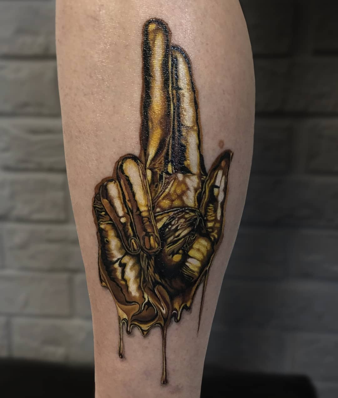 Realistic tattoo of a hand making the peace sign with gold, melting-like detail on a leg