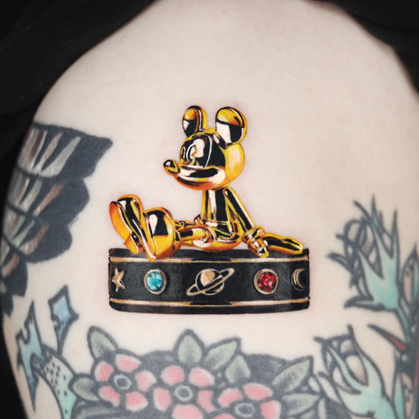 A tattoo featuring a golden mouse figure sitting atop a box with space-themed designs