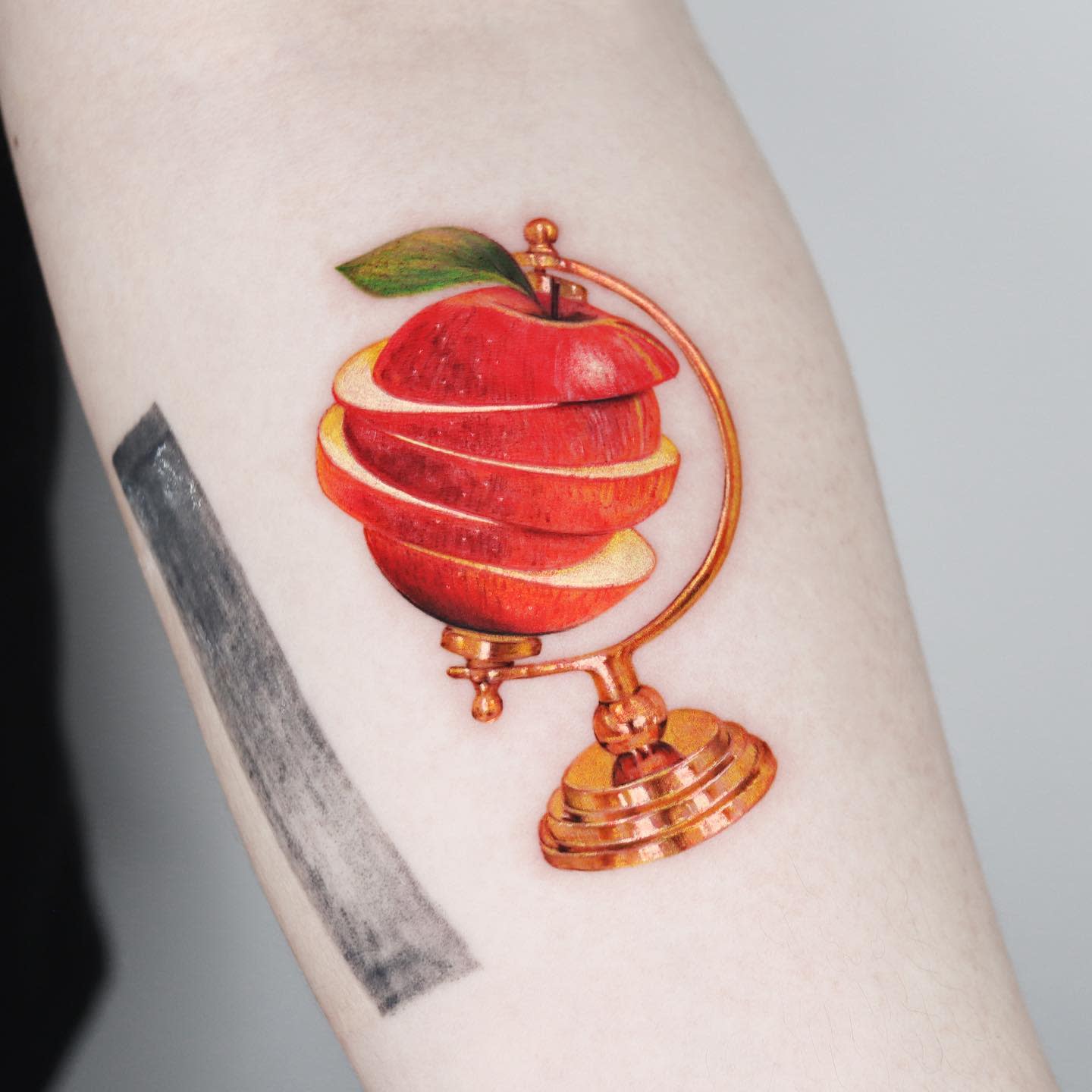 A tattoo of a sliced apple on a globe stand with a black rectangle beside it