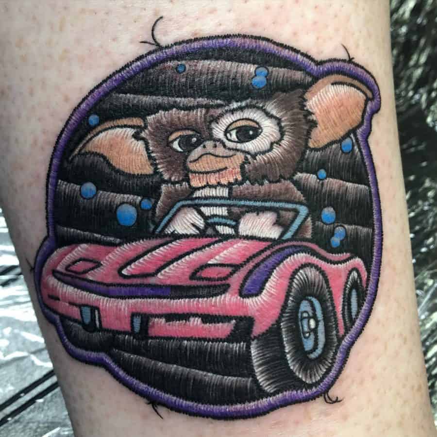 Realistic embroidered tattoo of a small, big-eared creature in a pink convertible, designed with thread-like textures for a 3D fabric look.