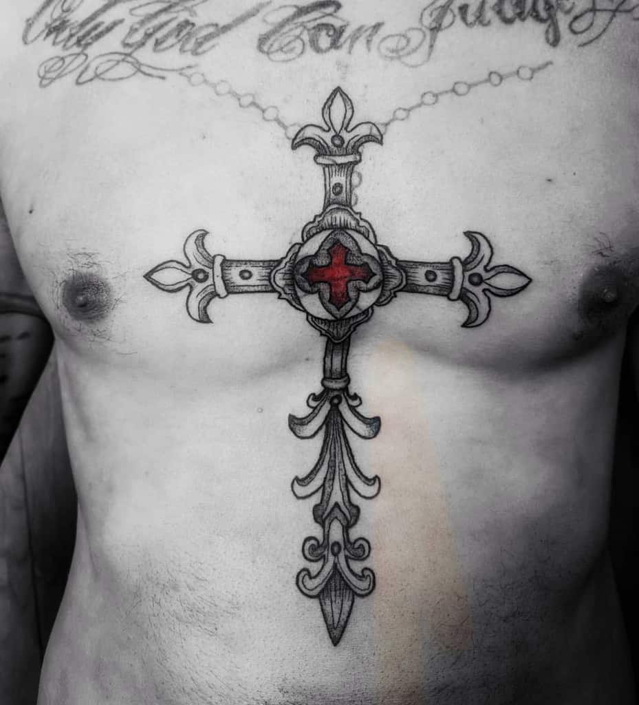 An ornate cross tattoo with a vivid red center graces the chest above the sternum