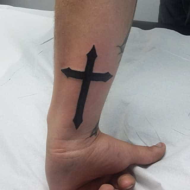 A bold, black cross tattoo adorns the forearm
