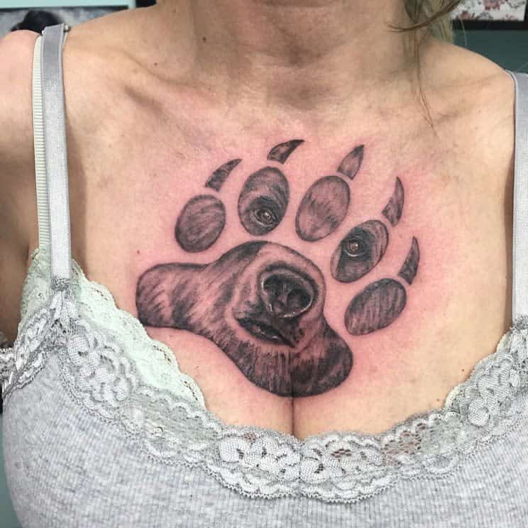 A dog's face within a bear paw on a woman's chest above a lace-trimmed top
