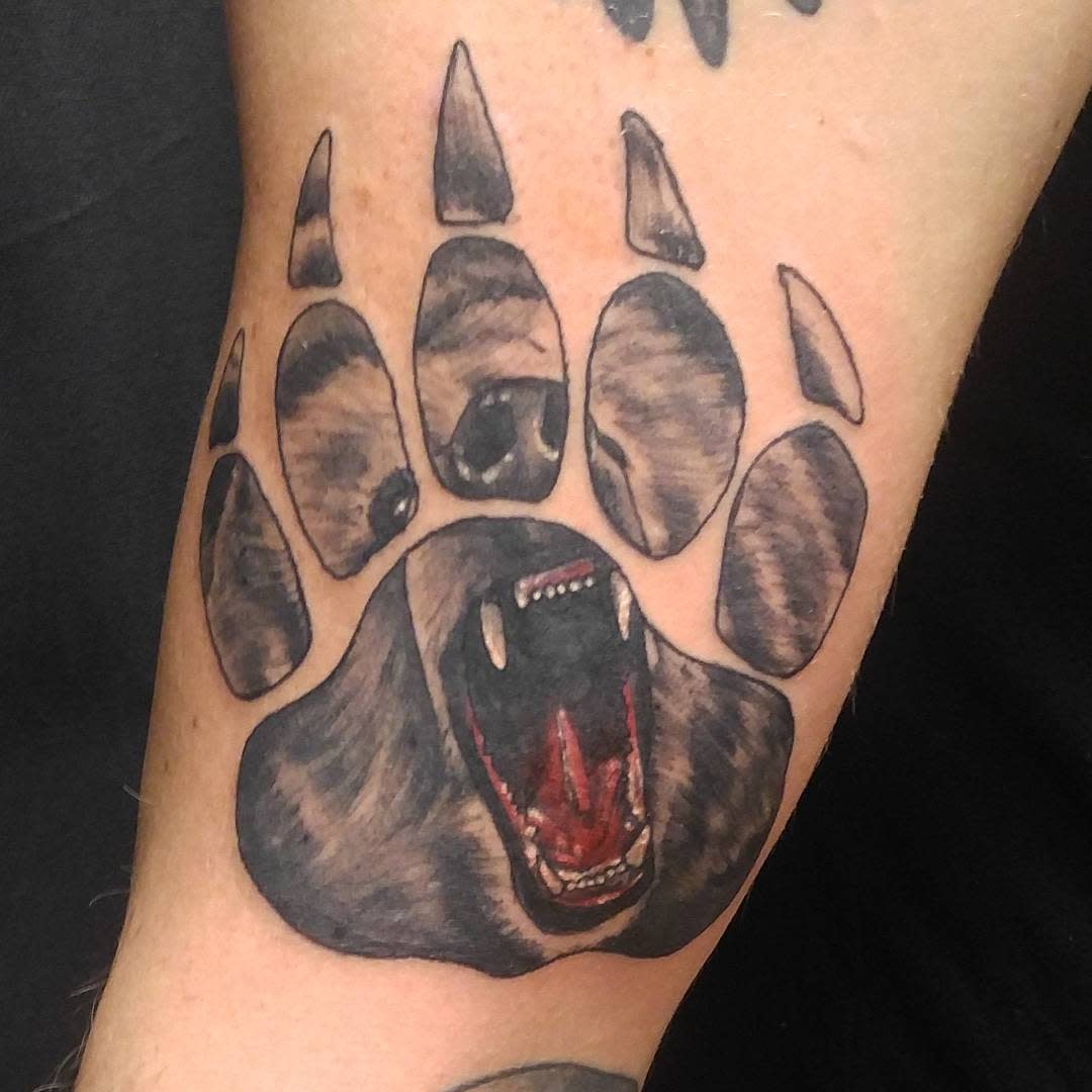 Tattoo of a bear's open mouth surrounded by bear paw prints on a person's arm