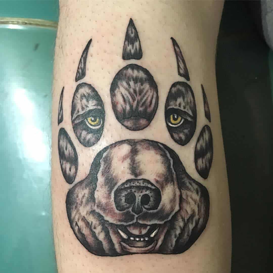 Tattoo of a bear paw with a bear's face intricately designed within it on a person's leg