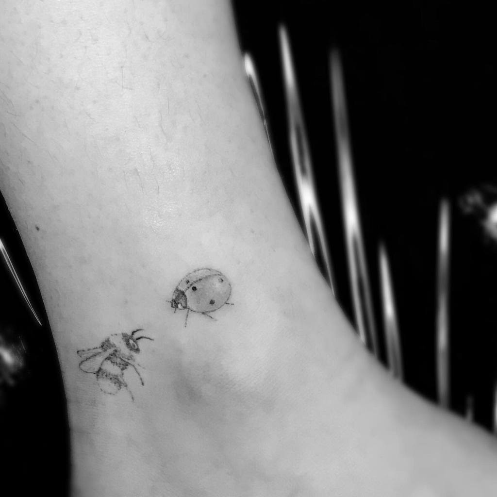 Black and white single needle tattoo of a bee and a ladybug on an ankle
