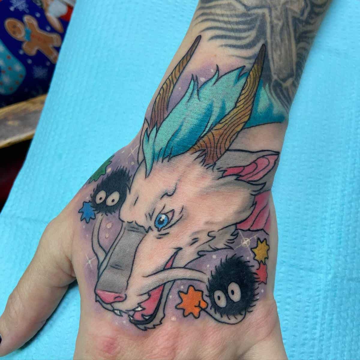 Vibrant tattoo of Haku and soot sprites from Spirited Away on the back of the hand