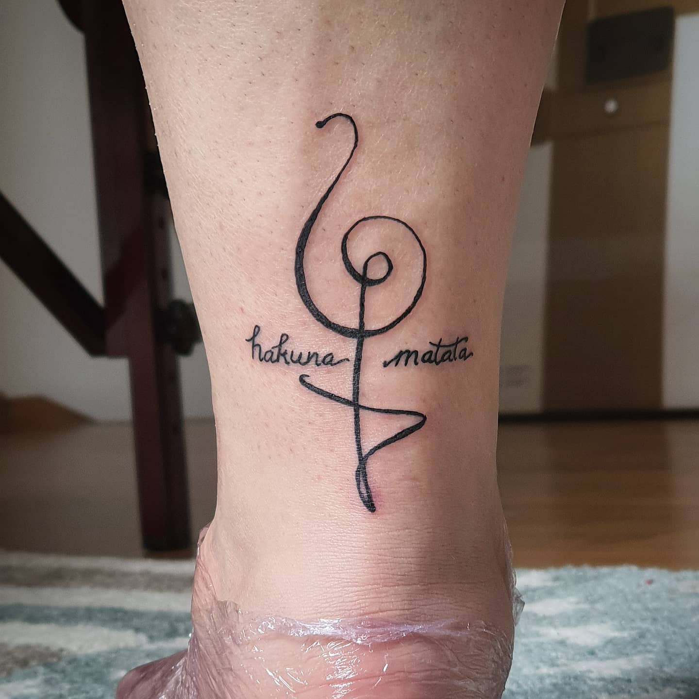 Tattoo on ankle featuring "hakuna matata" text and a stylized musical note design