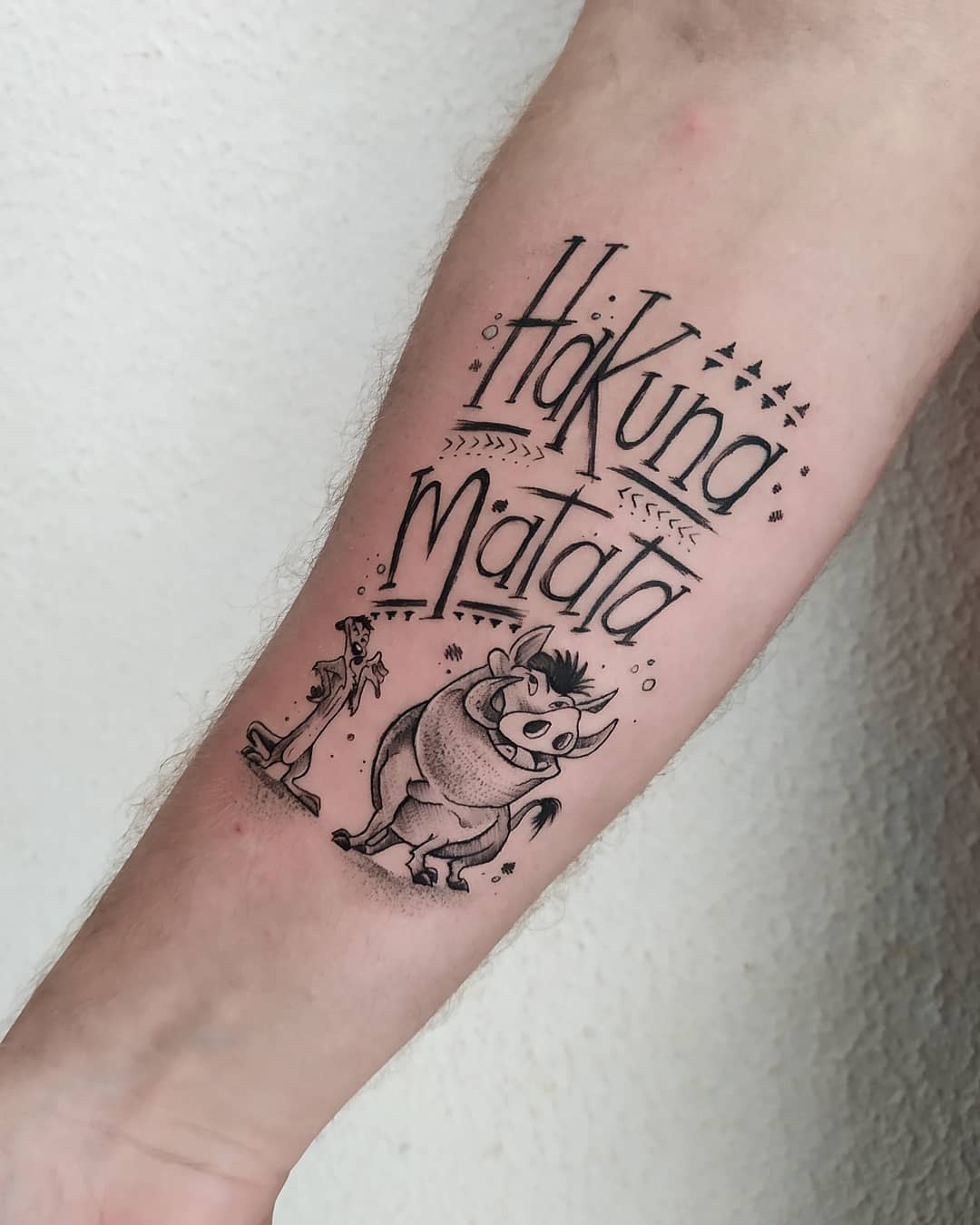Tattoo on forearm with "Hakuna Matata" and characters from The Lion King
