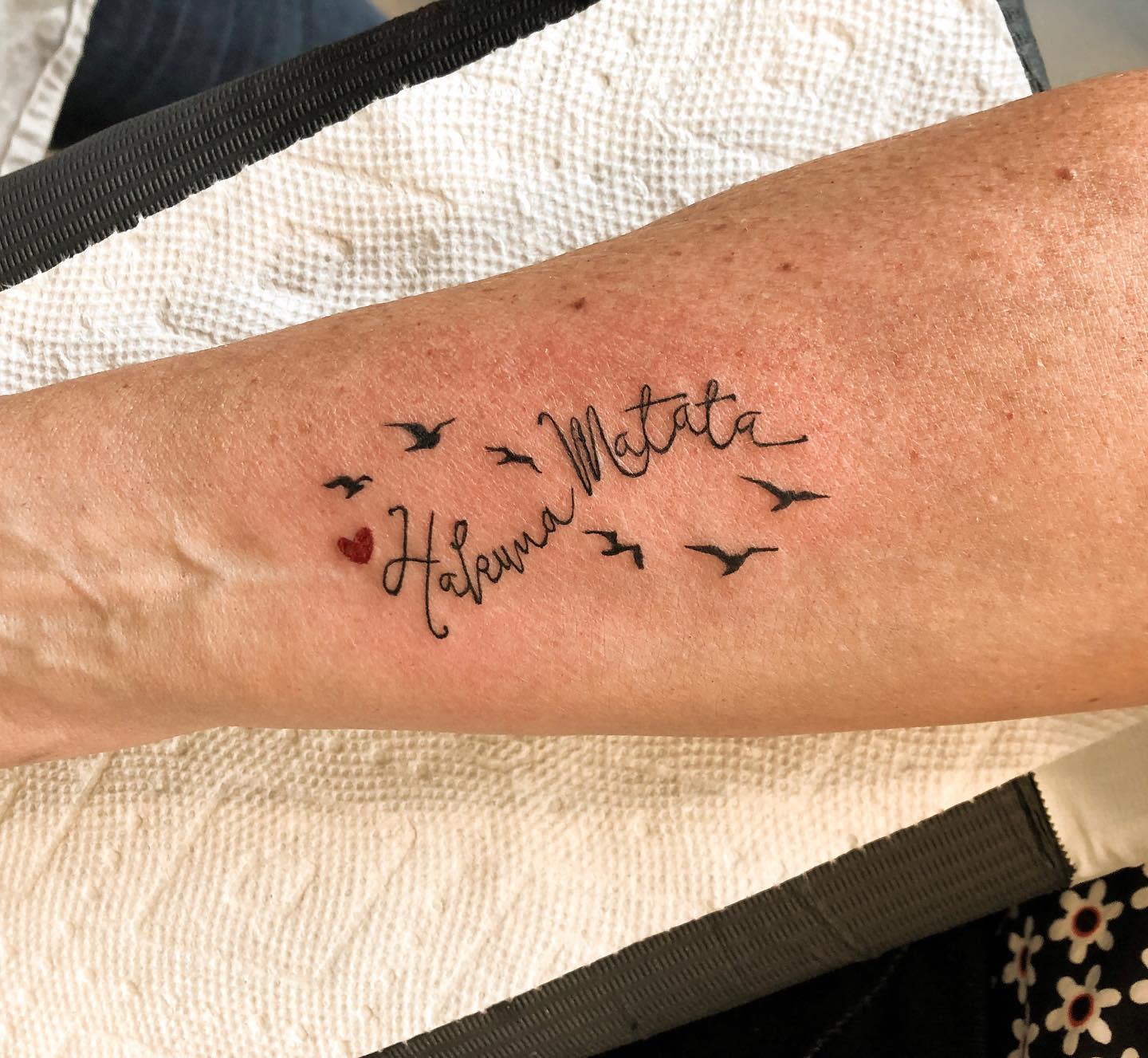 The tattoo on the forearm features the phrase "Hakuna Matata," accompanied by images of birds and a small red heart