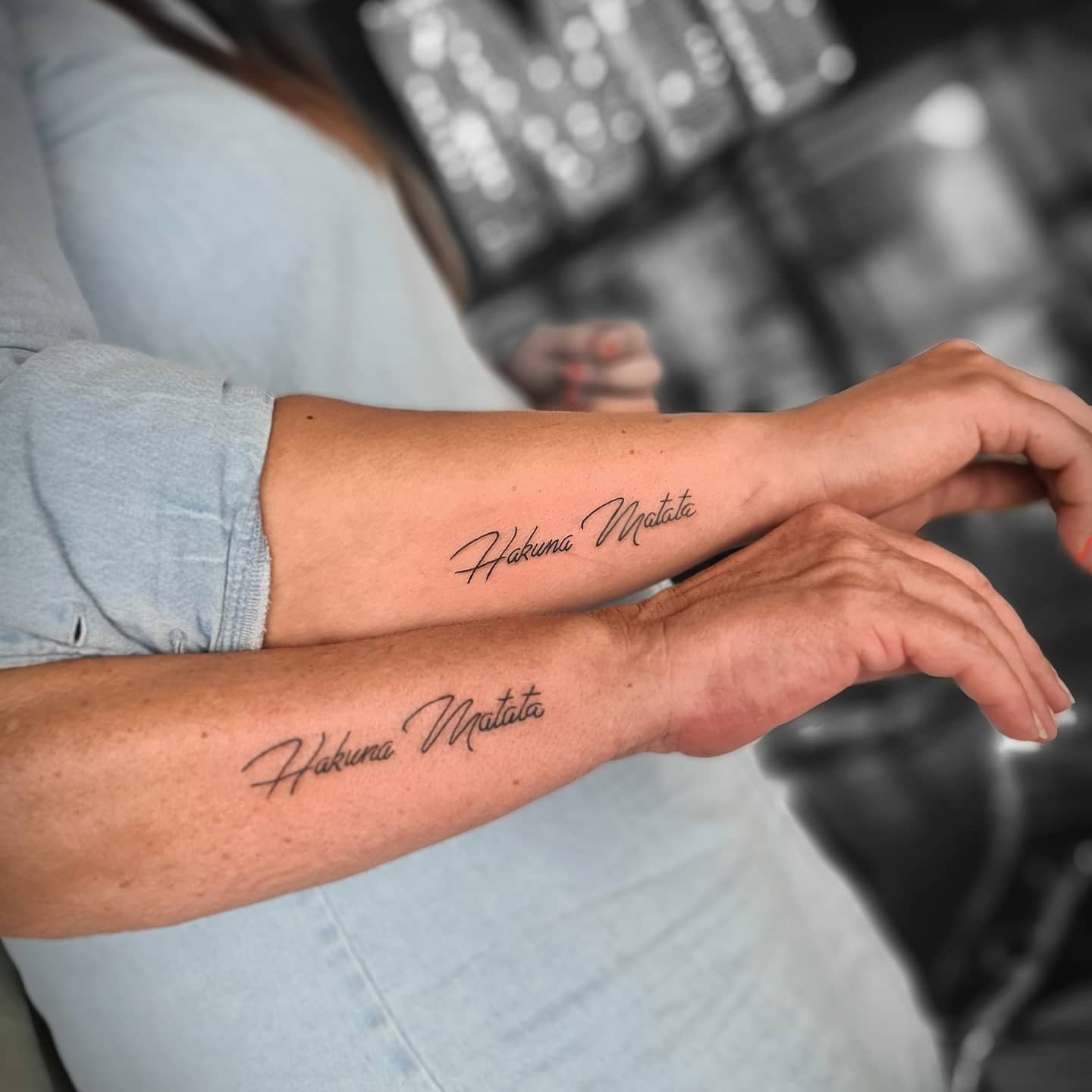 Two arms with matching tattoos that read "Hakuna Matata" in cursive script
