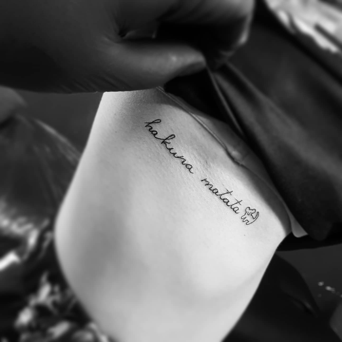 The tattoo features the phrase "hakuna matata" and a small drawing of a lion