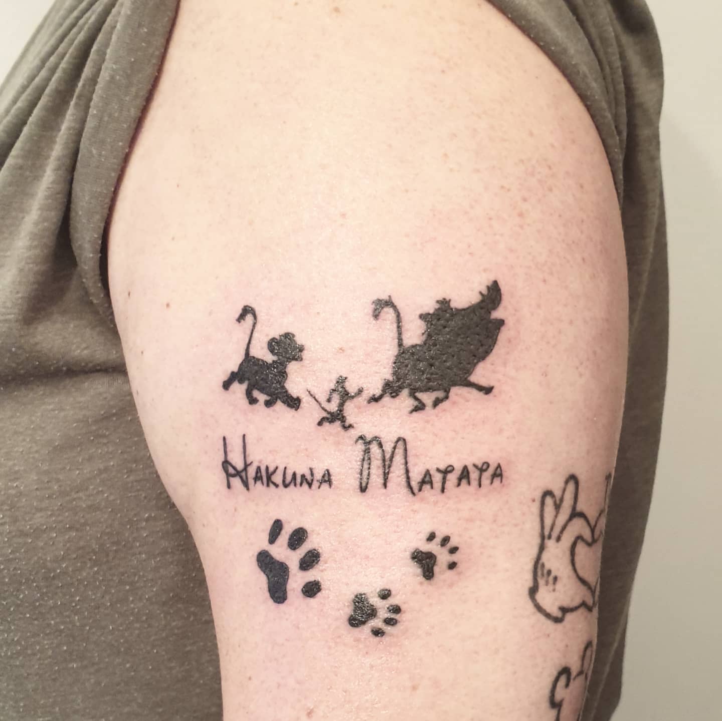 Tattoo on an arm of Lion King characters with the text "Hakuna Matata" and paw prints
