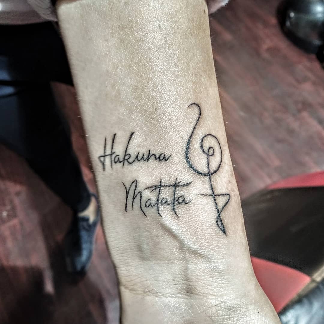 Tattoo on a wrist reading "Hakuna Matata" with a treble clef symbol replacing