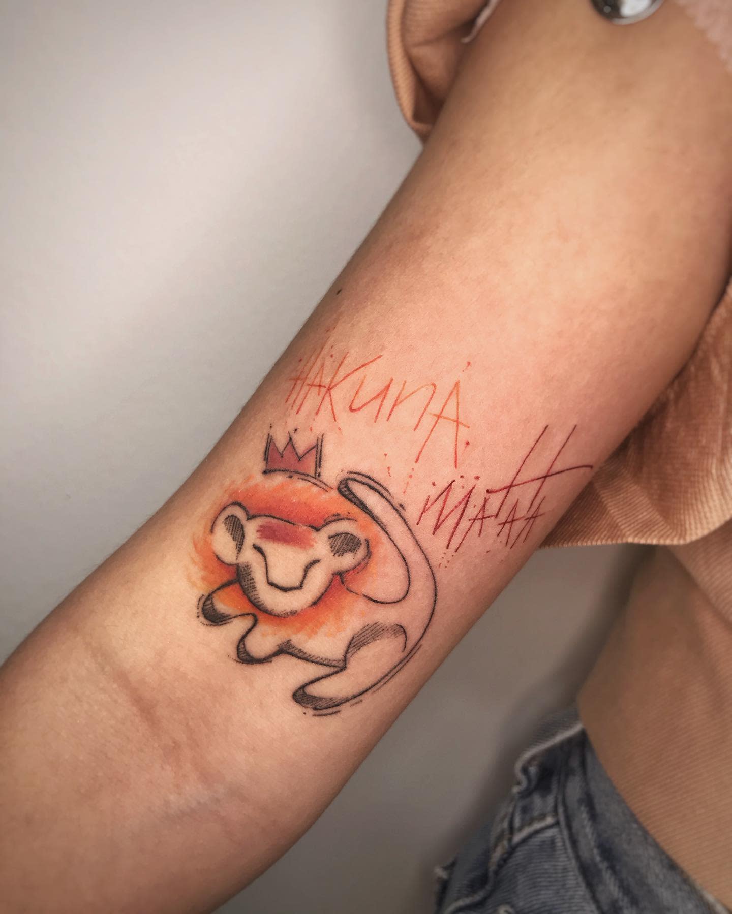 Artistic Hakuna Matata tattoo with a crowned lion cub and vibrant orange watercolor accents