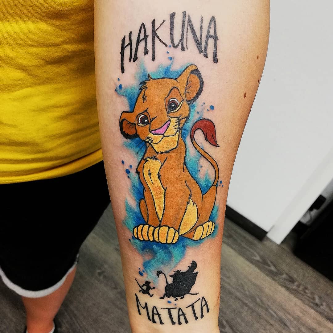 Tattoo of a young Simba and "Hakuna Matata" text on a forearm