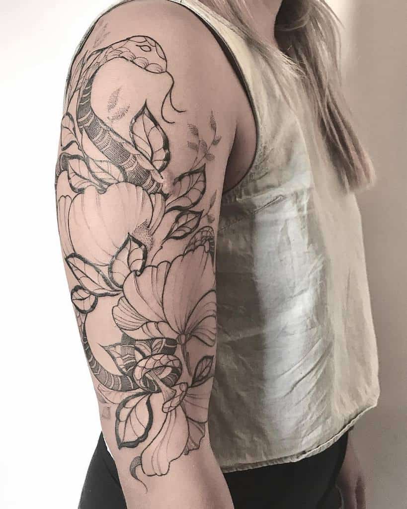 A woman's arm with a detailed black tattoo of flowers and a snake on her upper arm