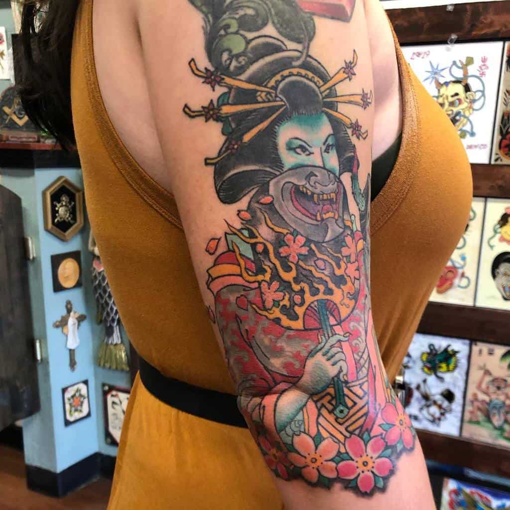 Colorful samurai-themed tattoo on a woman's arm, featuring a fierce face and intricate details