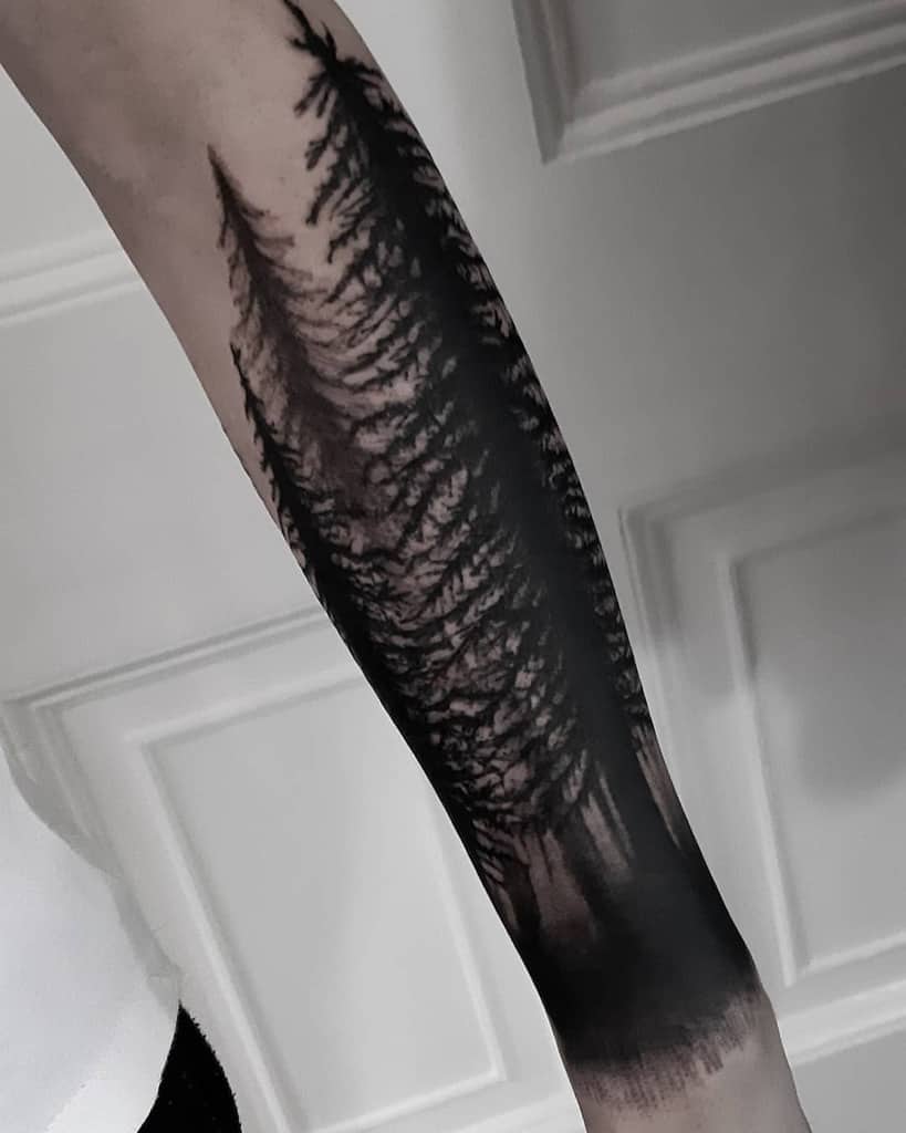 Arm with a detailed forest tattoo in black ink