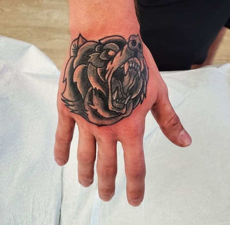 A hand with a meticulously detailed tattoo of a roaring bear on the back