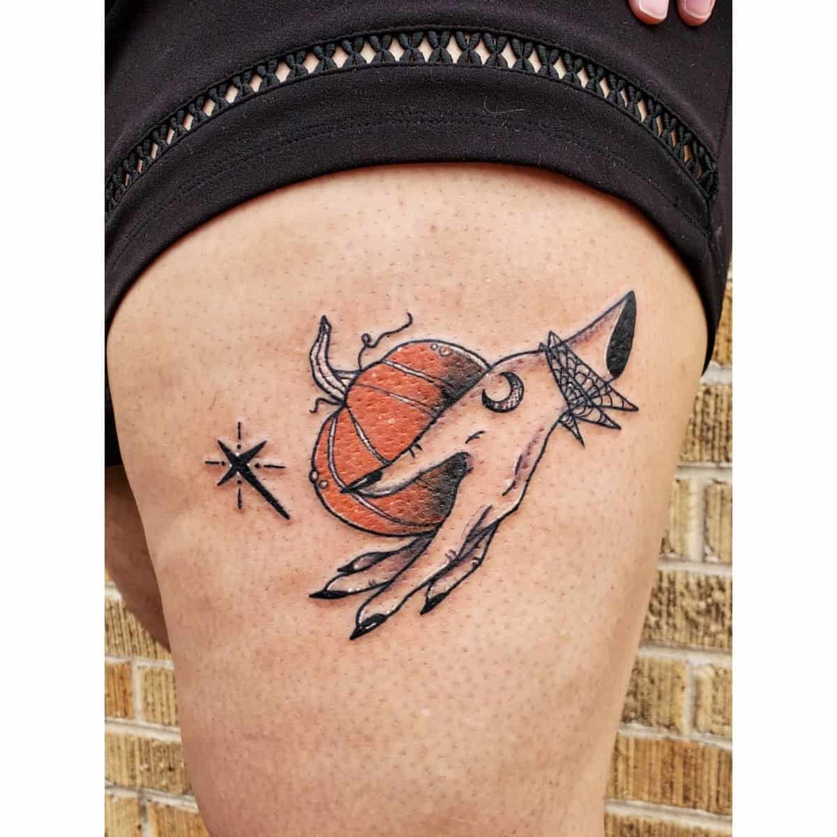 Witch's hand holding an orange orb with crescent moon and star tattoo on thigh