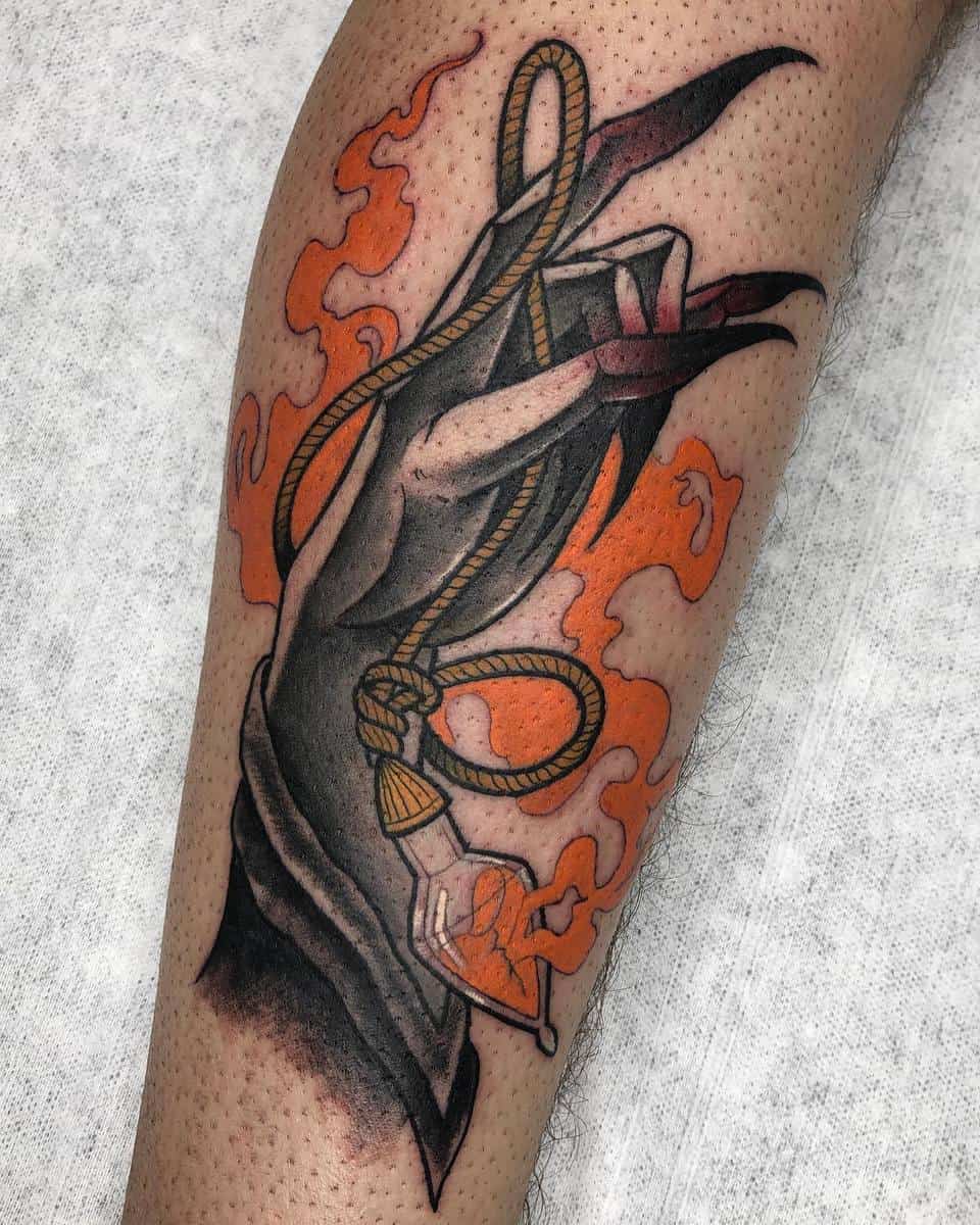Witch's hand holding a rope with a potion, surrounded by flames tattoo on leg