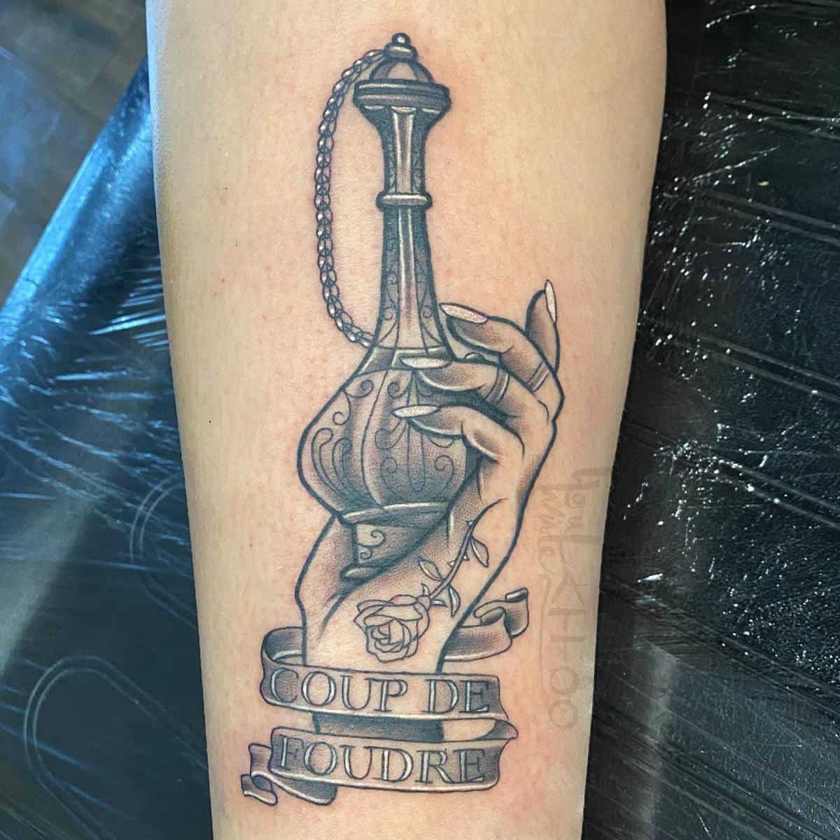 Tattoo of a hand holding a potion bottle with a ribbon that reads "COUP DE FOUDRE"
