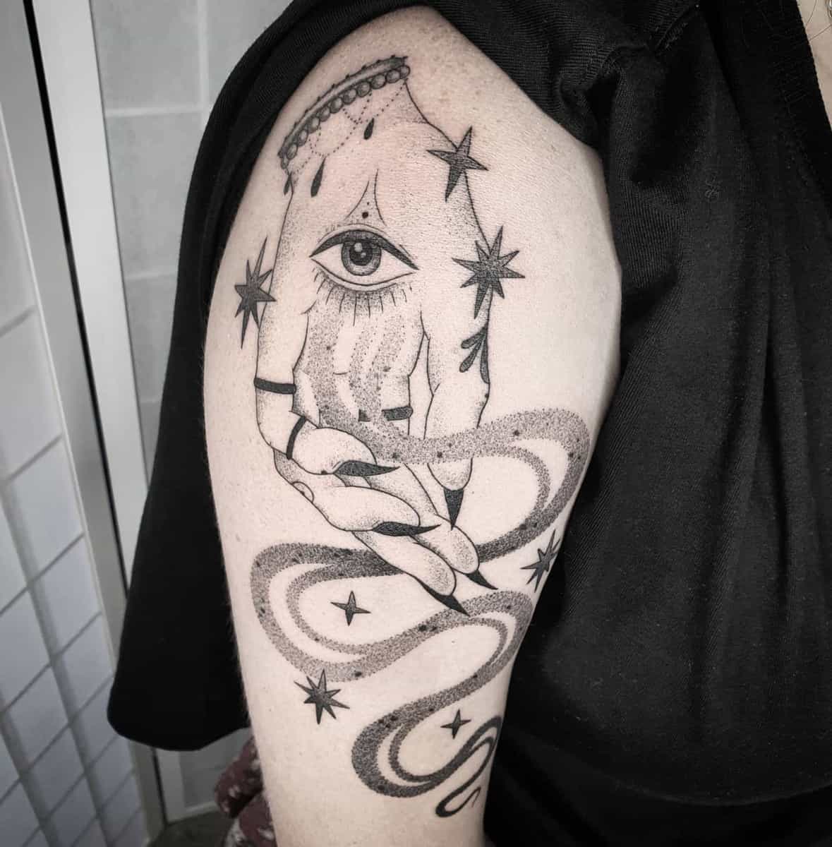 Black and gray tattoo of an eye in a hand with stars and swirling patterns on an arm