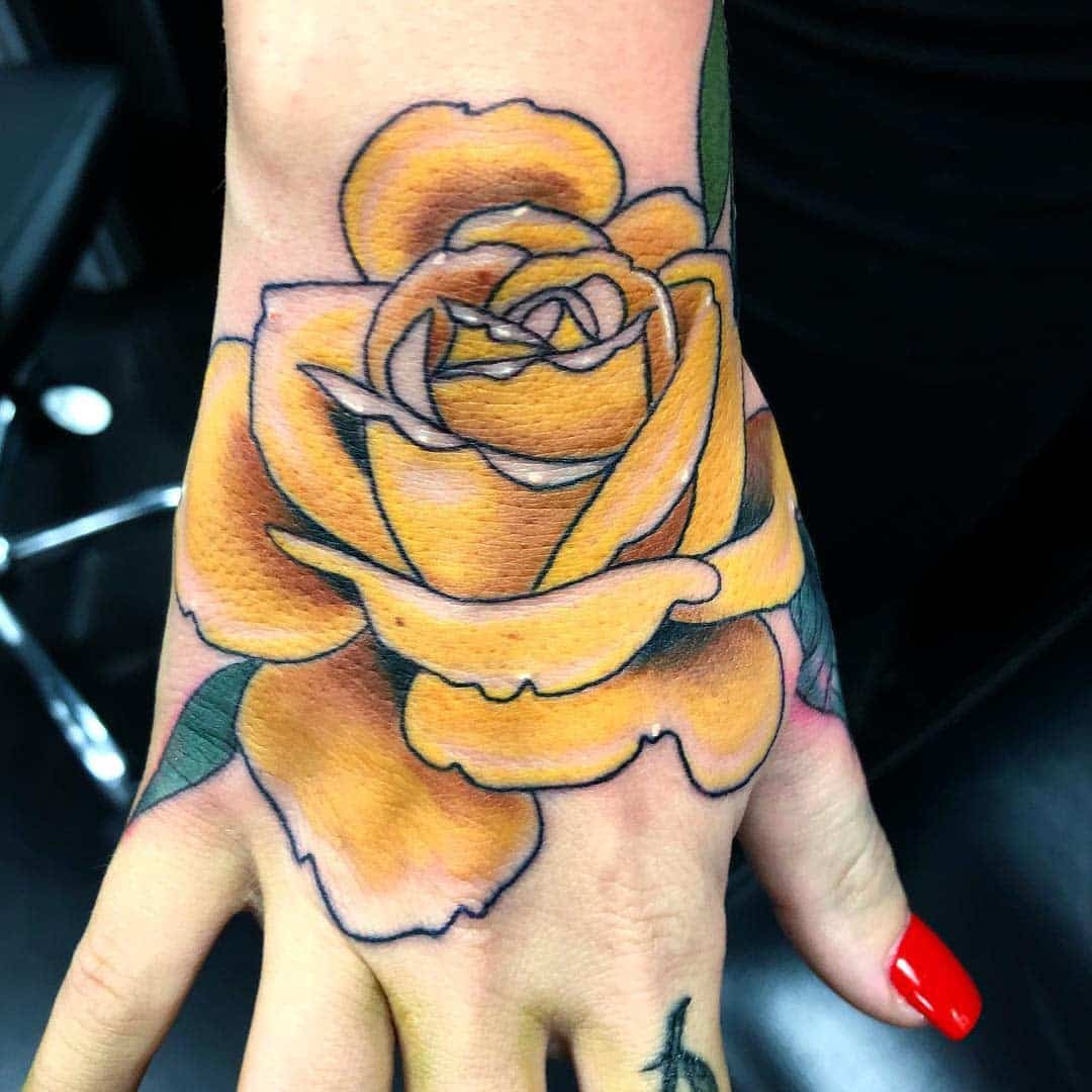 A vibrant yellow rose tattoo on the back of a hand, featuring detailed shading and green leaves