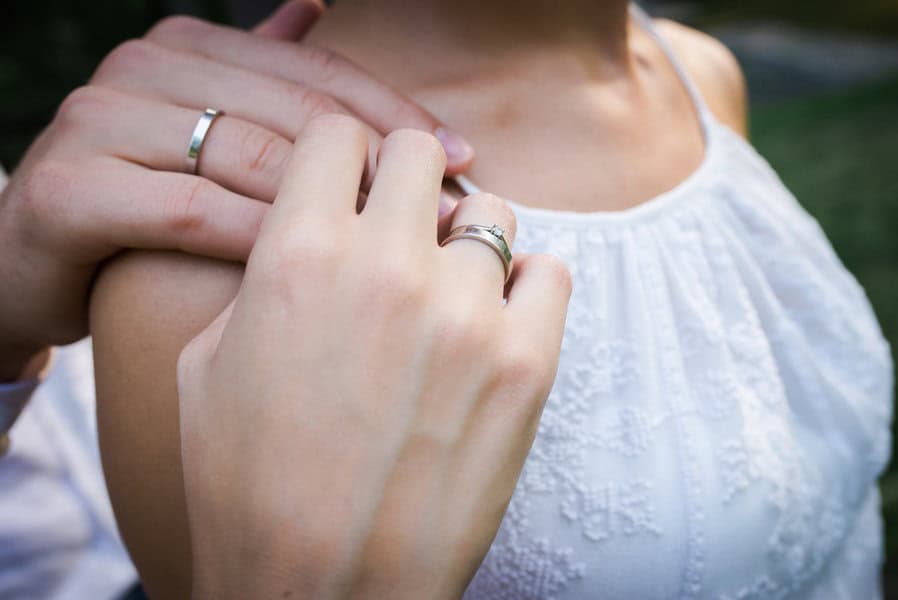 Close-up of two people in white, a hand rests on the other's shoulder, both feature fine gold rings for a subtle sense of modern luxury