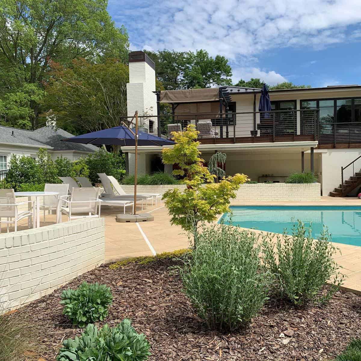 large backyard paver pool patio white outdoor furniture blue umbrella 