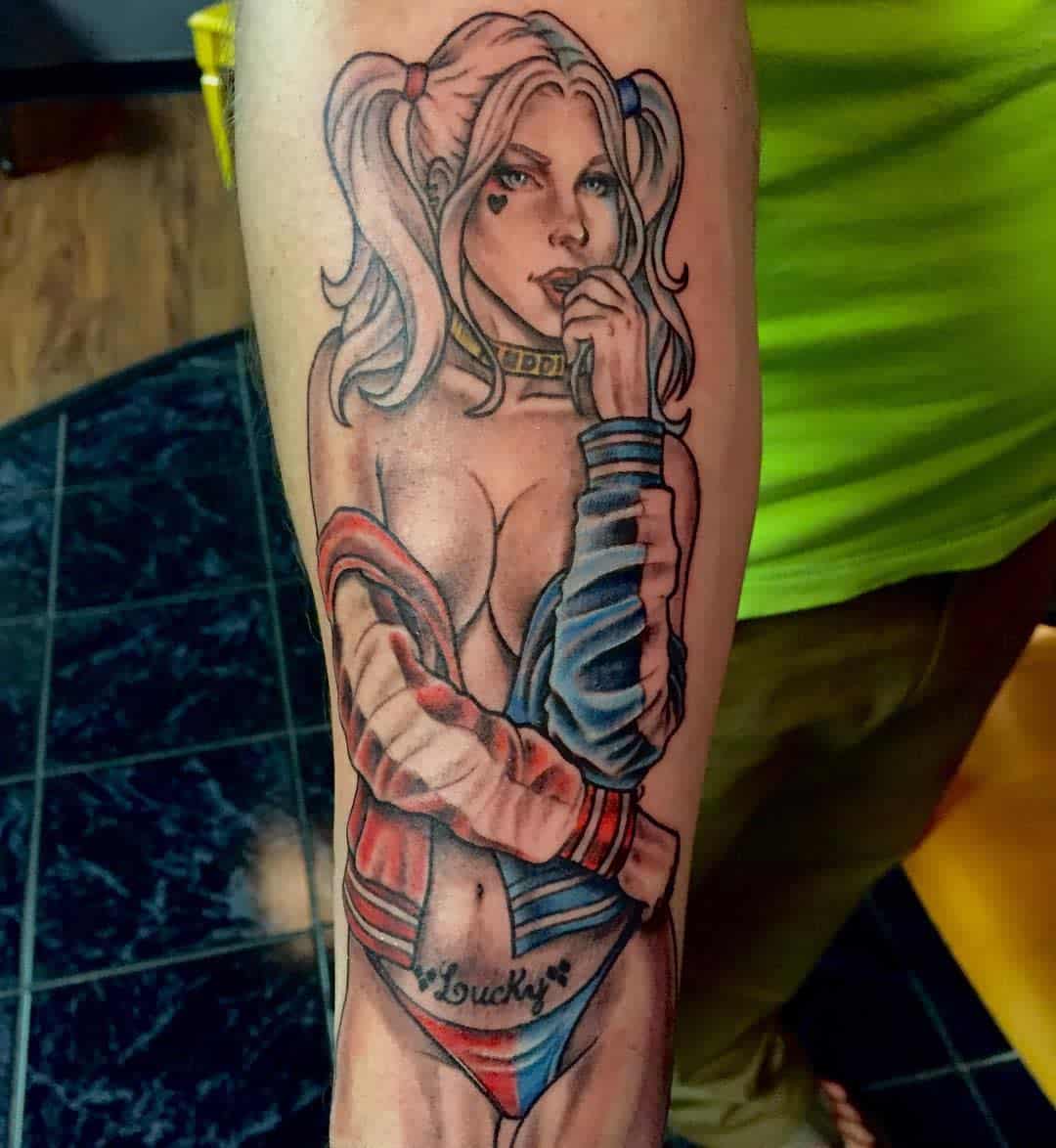 Tattoo of Harley Quinn in a seductive pin-up style, wearing a jacket and 'Lucky' underwear on the forearm